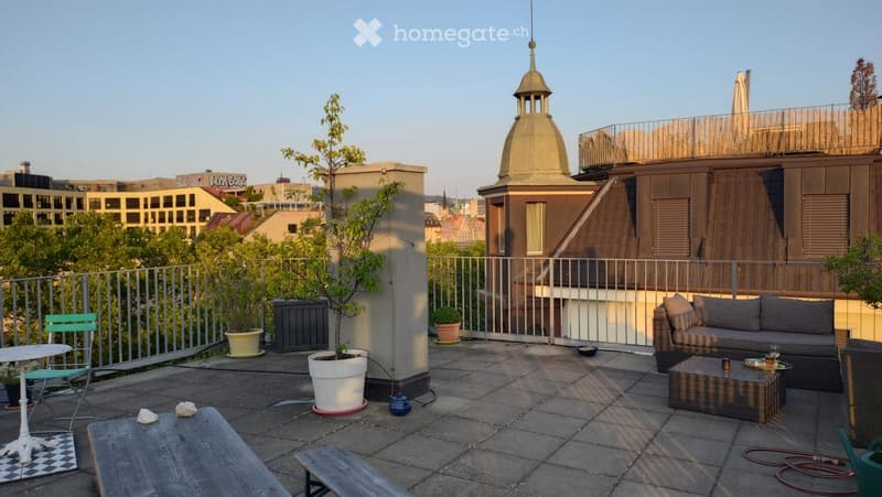 Rooftop terrace with a sofa, coffee table, chairs, small table, and potted plants, overlooking a cityscape with a dome-shaped building.