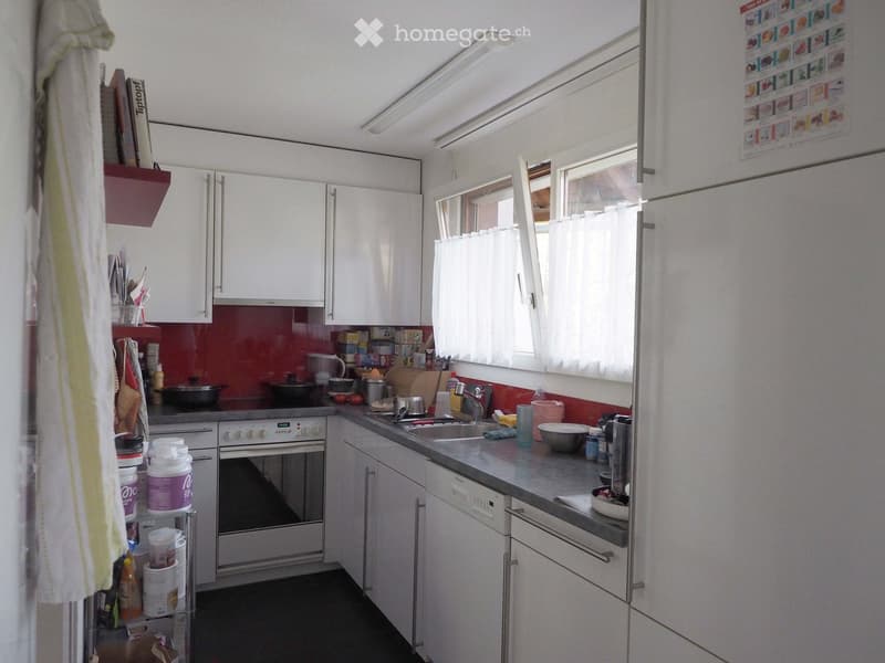 Modern kitchen with white cabinets, stainless steel appliances, and a red backsplash. Features include an oven, refrigerator, sink, and various kitchen items on the counter.
