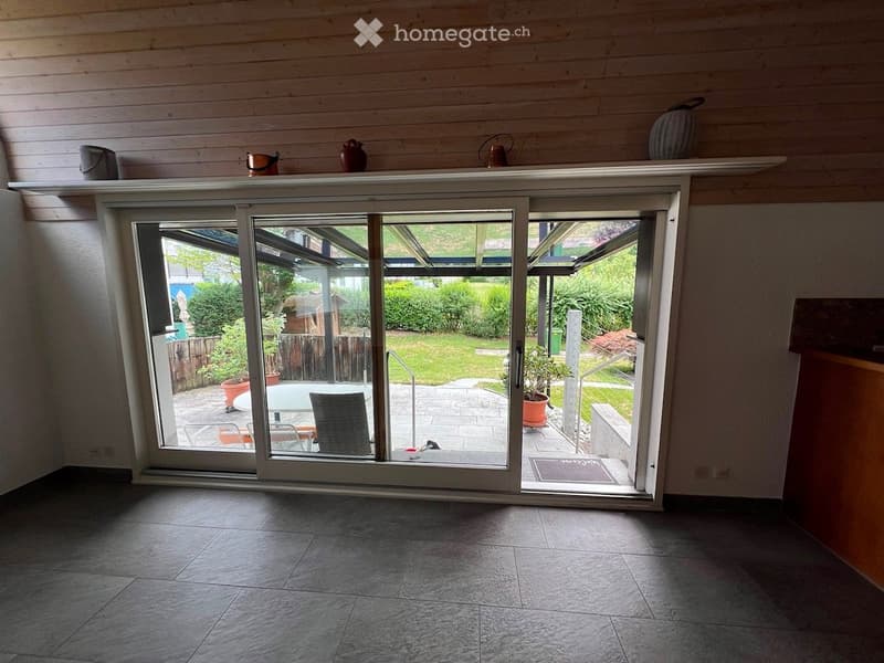 Bright hallway with large sliding glass doors leading to a patio area, wooden ceiling, tiled floor, and decorative items on a shelf above the doors.