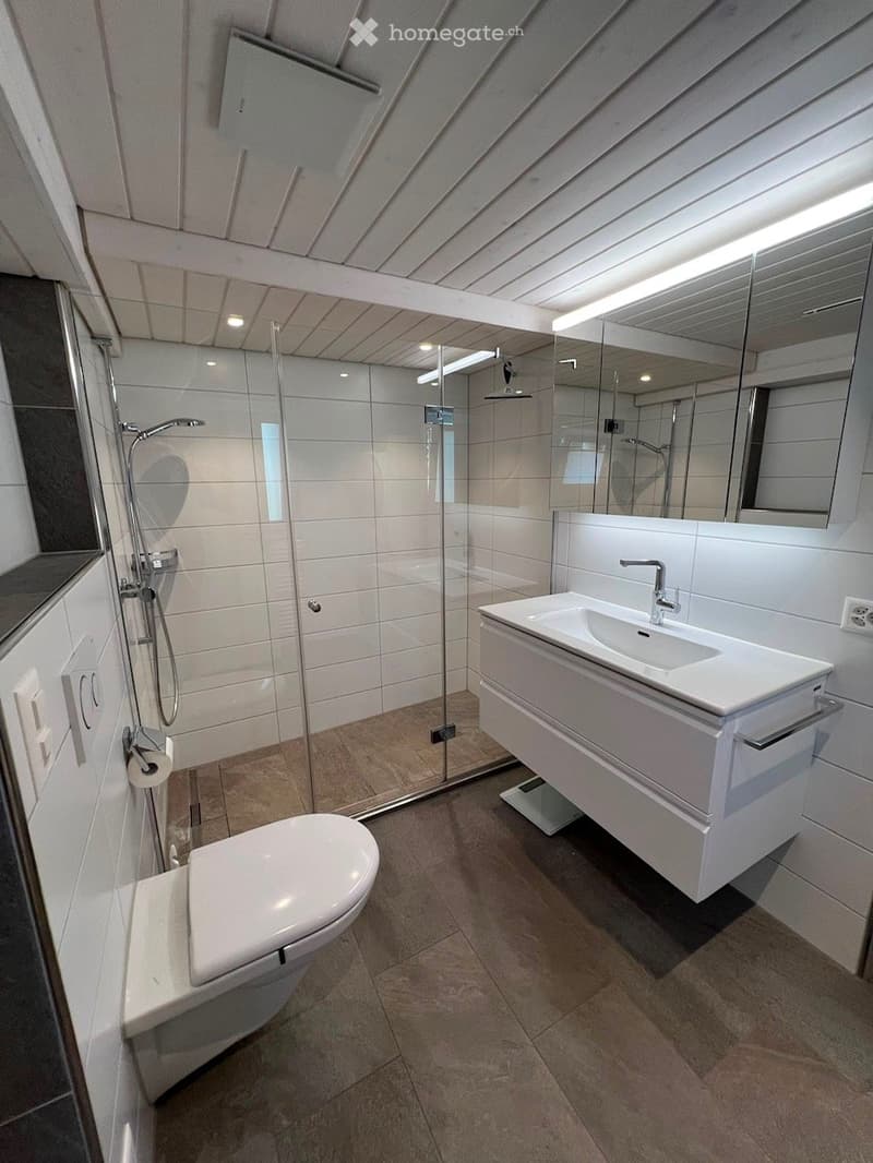 Modern bathroom with white tiles, a toilet, a sink with a mirror, and a glass-enclosed shower area.