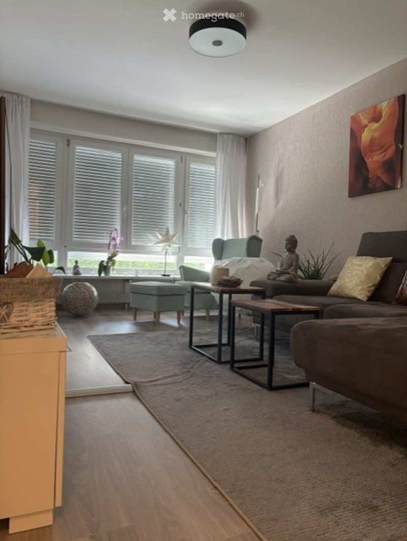 Modern living room with large windows, grey sofa, coffee tables, armchairs, ottoman, floor lamp, and decorative items.