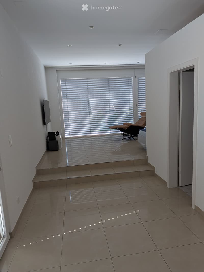 Modern, minimalistic room with large window, tiled floor, and a single chair near the window.