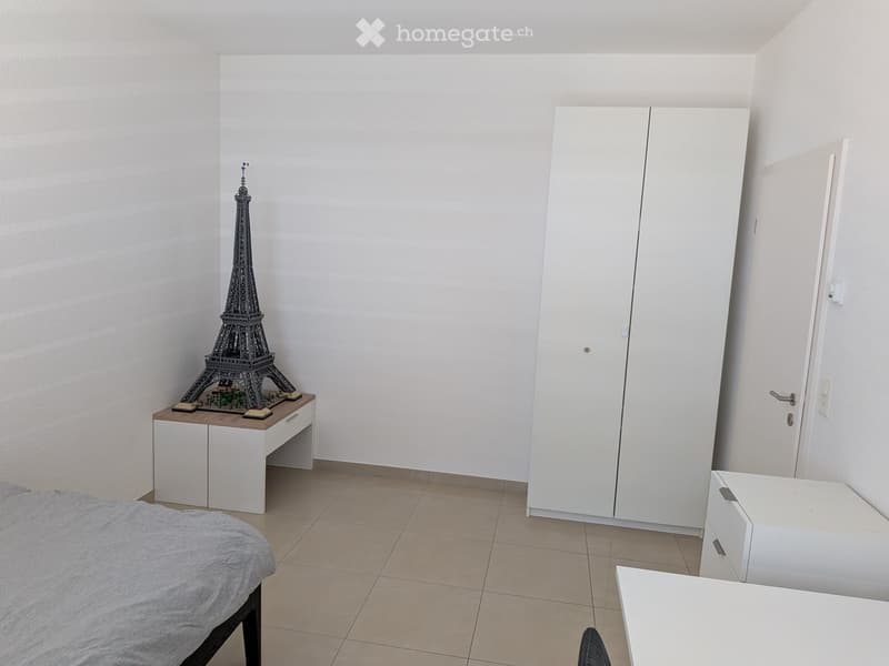 A modern, minimalist bedroom with a bed, nightstand, wardrobe, and a small table with a miniature Eiffel Tower model on it.