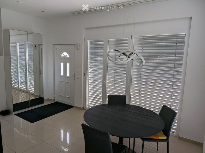 Modern dining area with a round wooden table, four chairs, a large mirror, and a contemporary hanging light fixture.