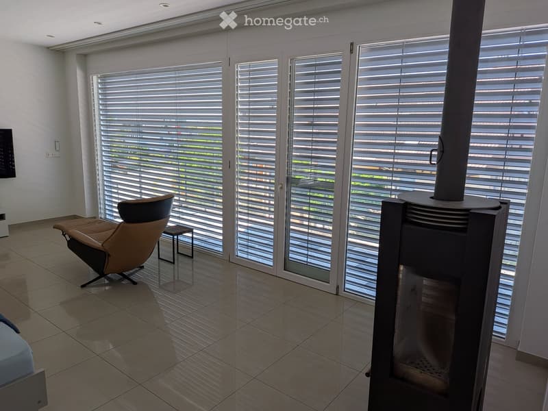 Modern living room with large windows, a fireplace, a comfortable chair, and a small side table.