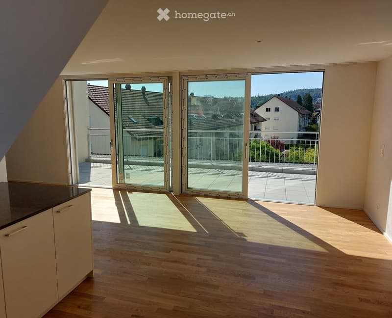 Bright, empty room with wooden flooring and large sliding glass doors leading to a balcony with a view of the neighborhood.