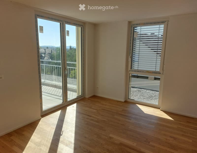 Empty room with wooden flooring, large sliding glass door leading to a balcony, and a window with blinds.