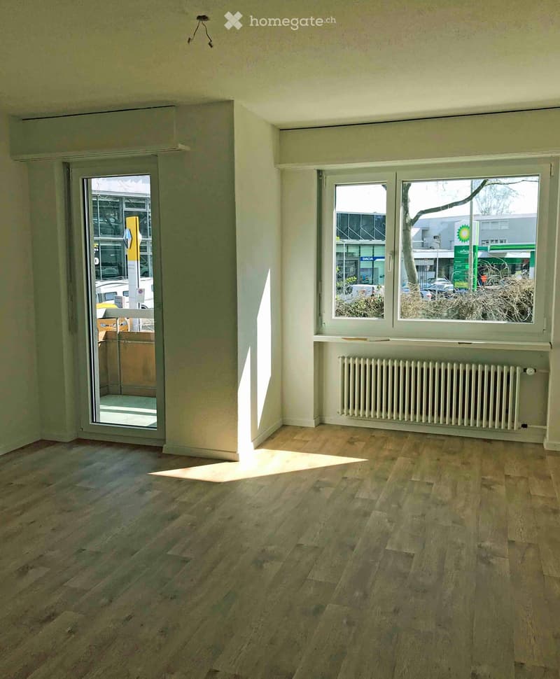 Empty room with wooden flooring, large windows, radiator, and a sliding glass door leading outside.
