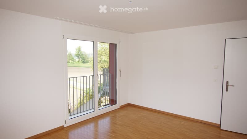Empty room with light-colored walls, wooden flooring, and a sliding glass door leading to a balcony.