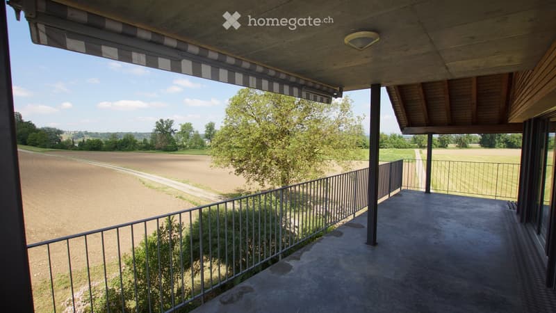 Balcony with metal railing, wooden ceiling, and a view of a rural landscape with fields and trees.