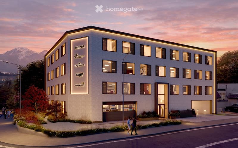Modern multi-story building with illuminated signage, large windows, and a well-maintained entrance area with landscaping and a paved walkway.