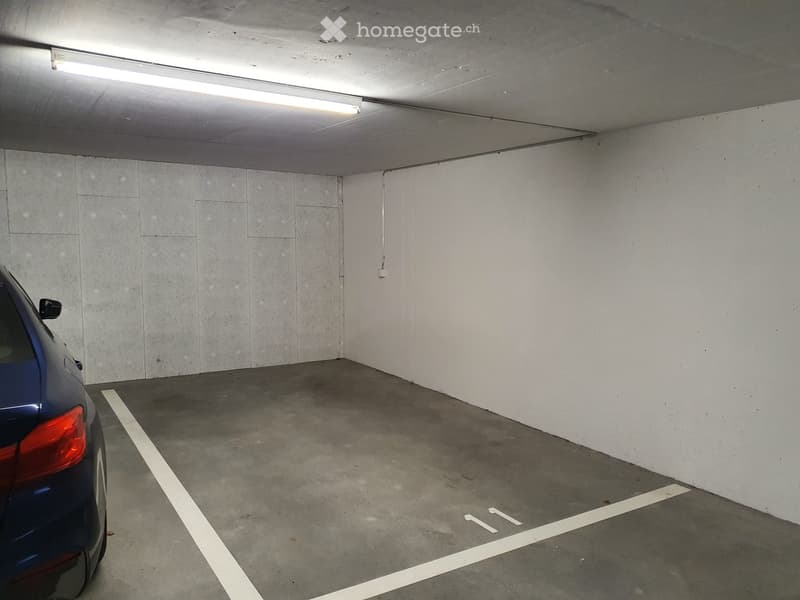 Underground parking space with a single car parked, marked parking spaces, and fluorescent lighting.