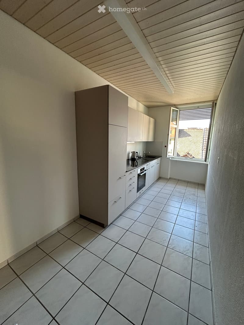 Modern kitchen with white cabinets, tiled floor, and a window overlooking a roof area.