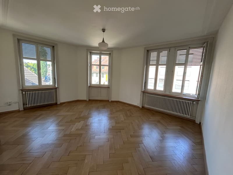 Empty room with wooden herringbone flooring, large windows with shutters, radiators, and a hanging light fixture.