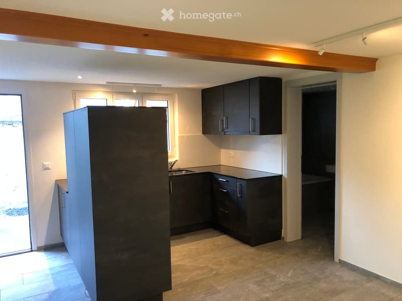 Modern kitchen with dark cabinets, stainless steel sink, and a large refrigerator. The space features a tiled floor and recessed lighting.