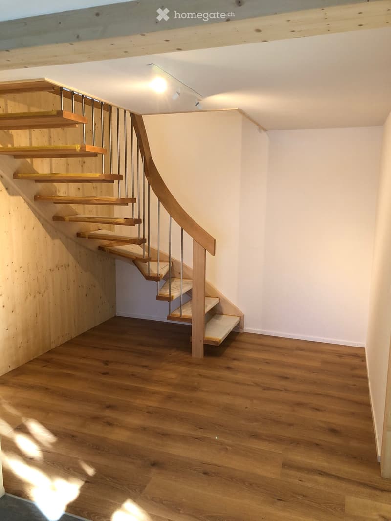Modern wooden staircase with metal railing, light wooden floors, white walls, and recessed lighting.