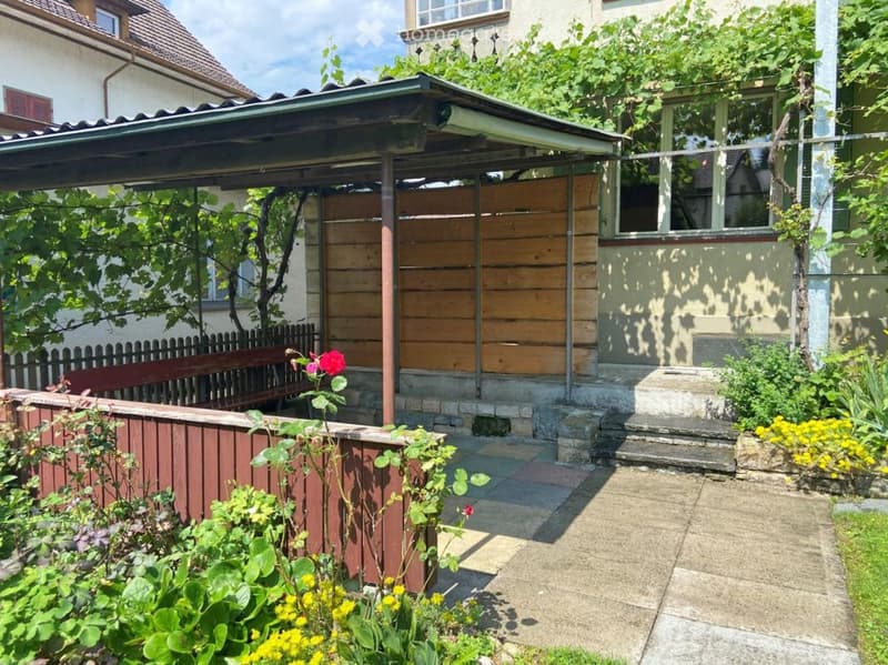 Garden area with a wooden pergola, steps leading to a house, flowers, and a bench.