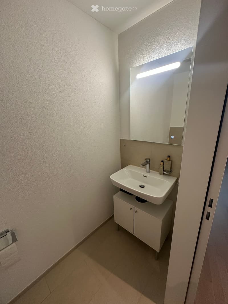 Modern bathroom with a white sink, mirror with built-in lighting, and a small cabinet underneath.