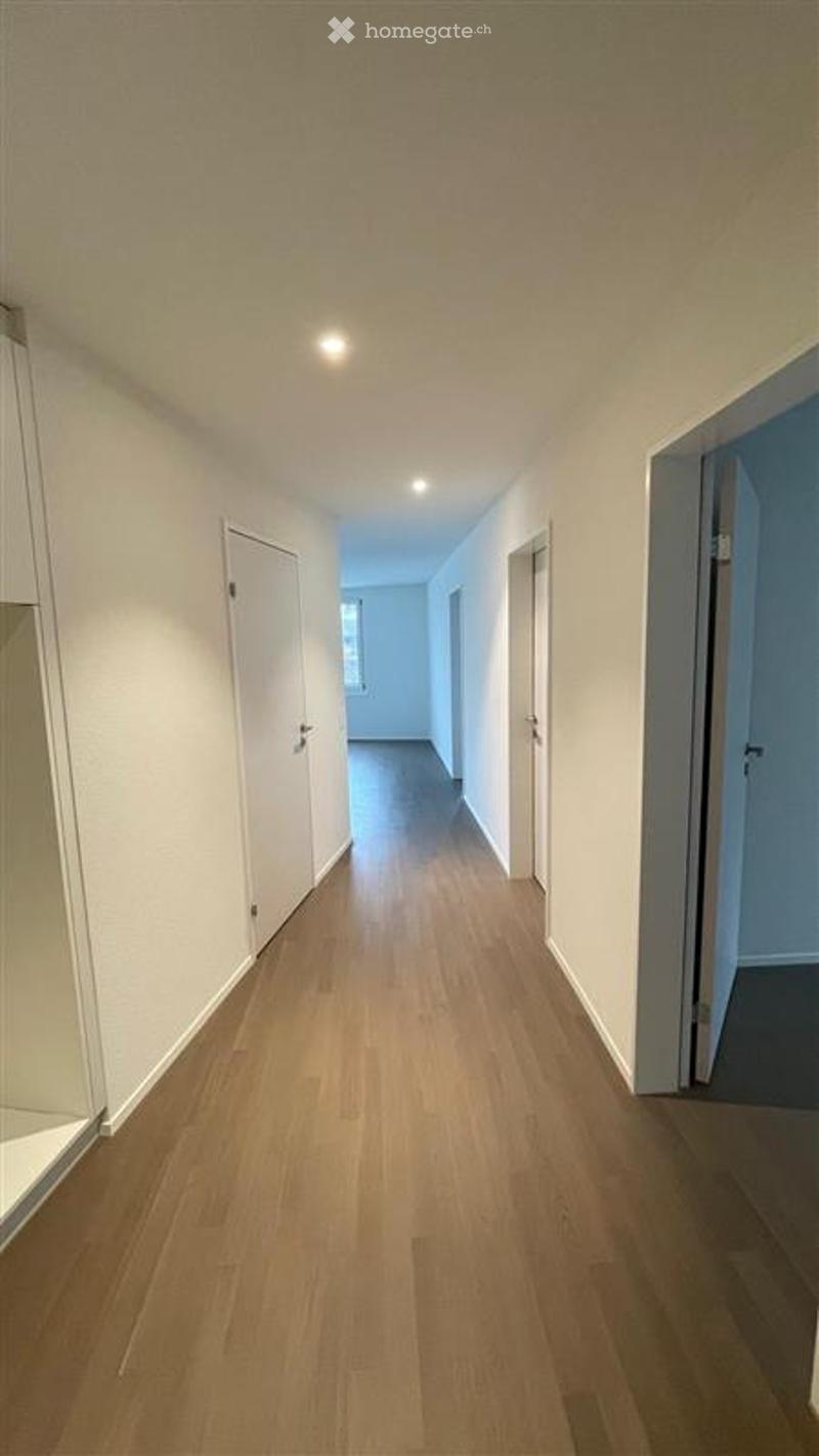 Empty hallway with light wooden flooring, white walls, and several closed doors on both sides.