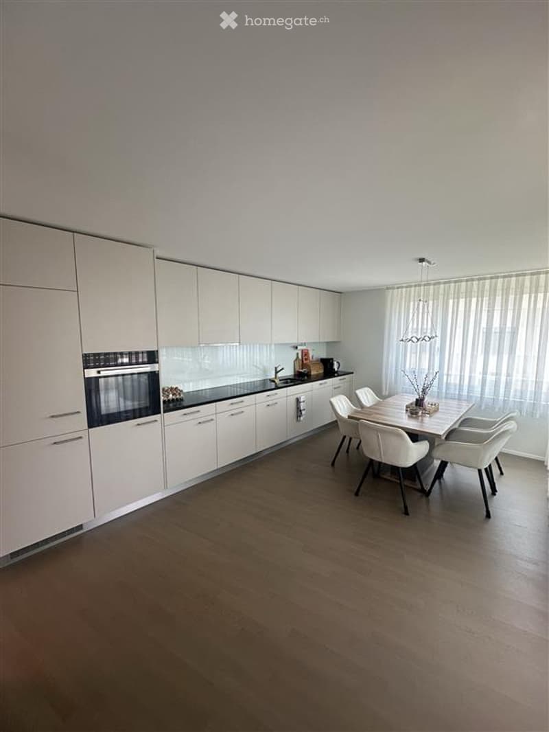 Modern kitchen with white cabinetry, black countertops, and a built-in oven. A dining area with a table and chairs is adjacent to the kitchen.