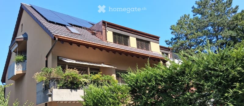 Two-story house with solar panels on the roof, balconies, and surrounding greenery.