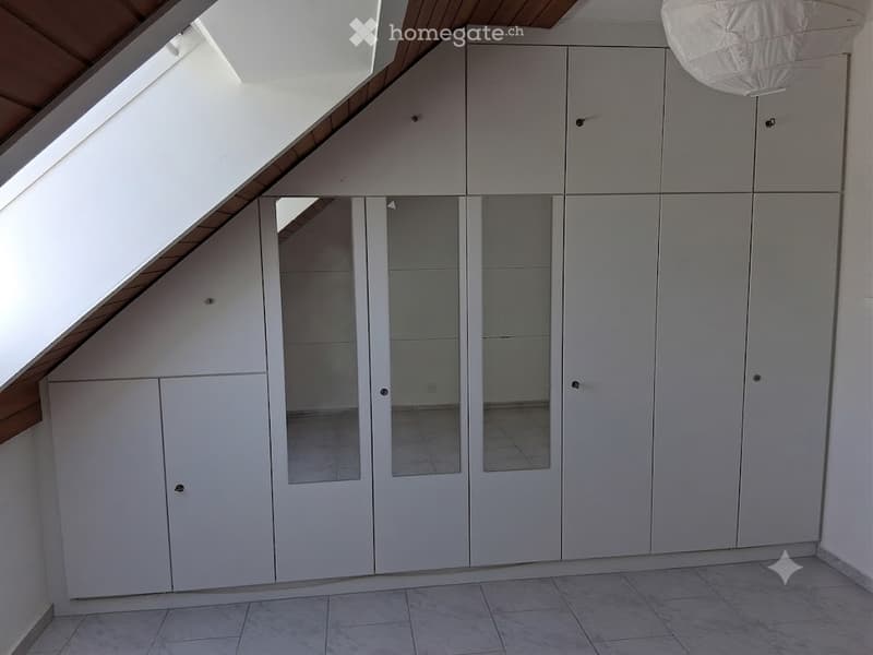 Empty room with white built-in wardrobes, tiled floor, and skylight window.