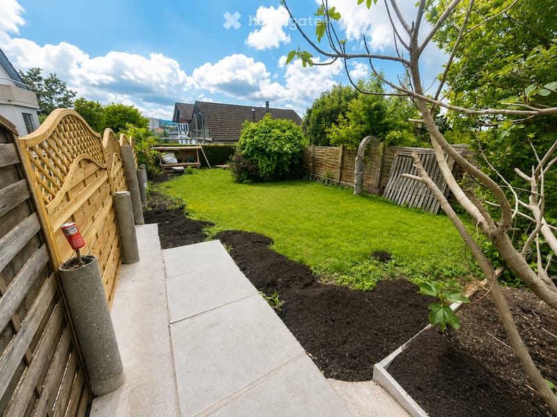 Garden with a paved pathway, wooden fence, concrete planters, and a well-maintained lawn.