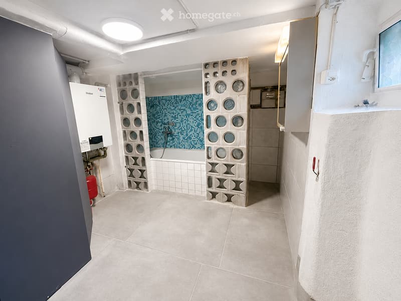 Modern bathroom with a bathtub, tiled walls, a water heater, and a cabinet. The space features a clean, contemporary design with a mix of white and blue tiles.
