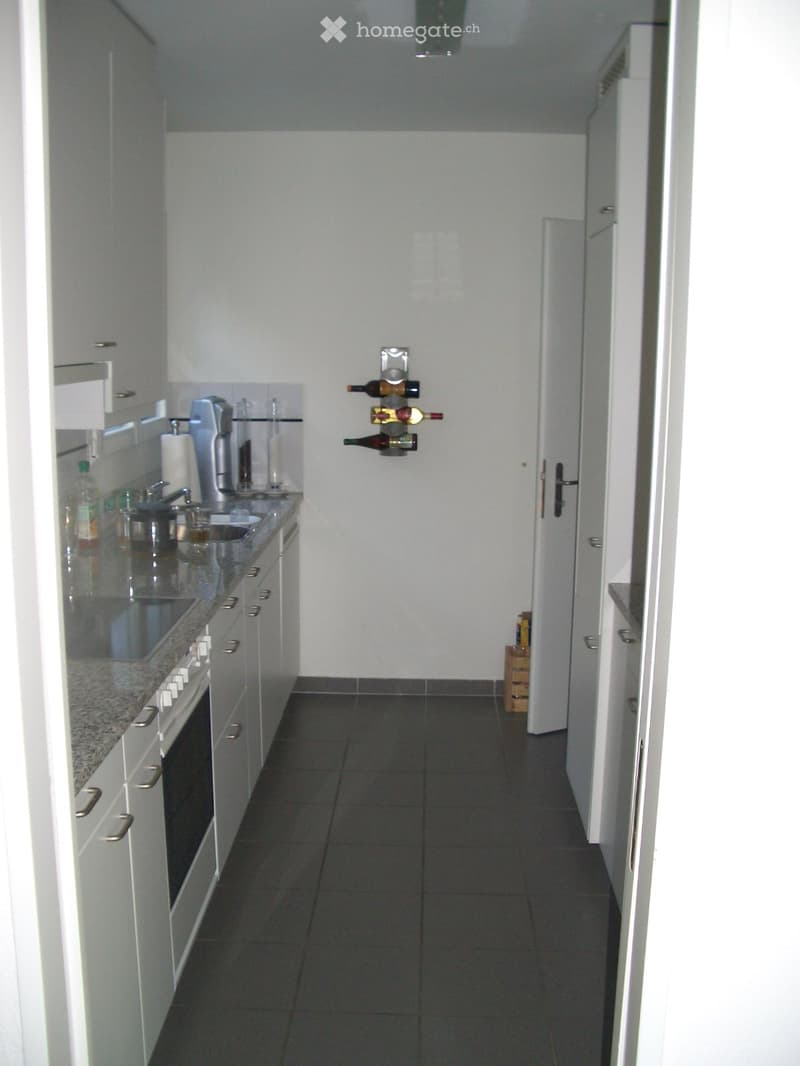 Modern kitchen with white cabinets, granite countertop, sink, oven, wine rack, and various kitchen items.