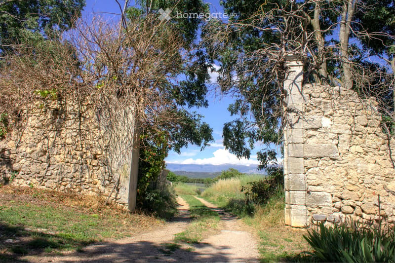 A rustic stone pathway flanked by stone walls, with trees and a scenic view of the countryside in the background.