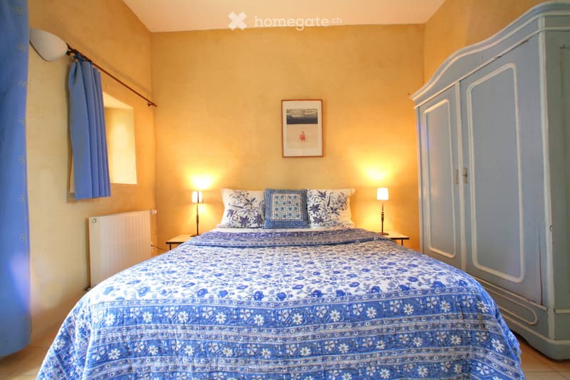Cozy bedroom with a double bed, nightstands, lamps, and a large wardrobe. The walls are painted a warm yellow, and there is a framed picture on the wall.