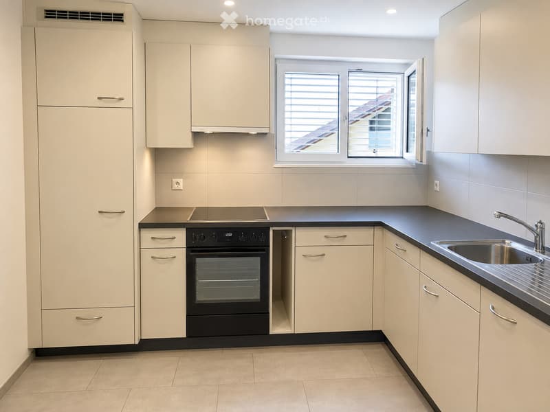 Modern kitchen with white cabinets, black countertop, stainless steel sink, and built-in oven. Features a window with blinds and recessed lighting.