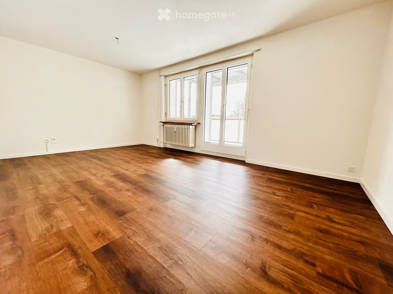 Empty room with wooden flooring, white walls, large windows, and a radiator under one window.