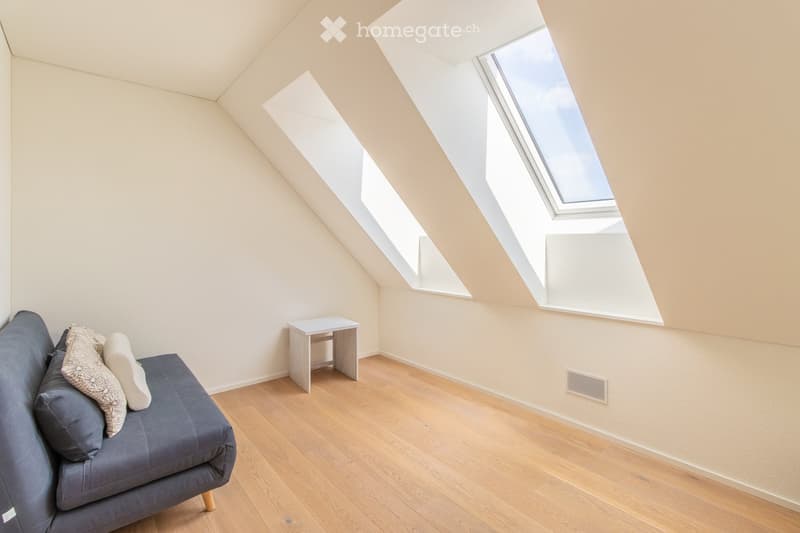 Bright attic room with wooden flooring, grey sofa, small table, and skylight windows.