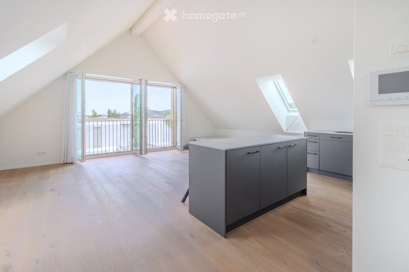 Modern kitchen with grey cabinets, a central island, and a microwave mounted on the wall. The space features wooden flooring and large windows with a view of the balcony.