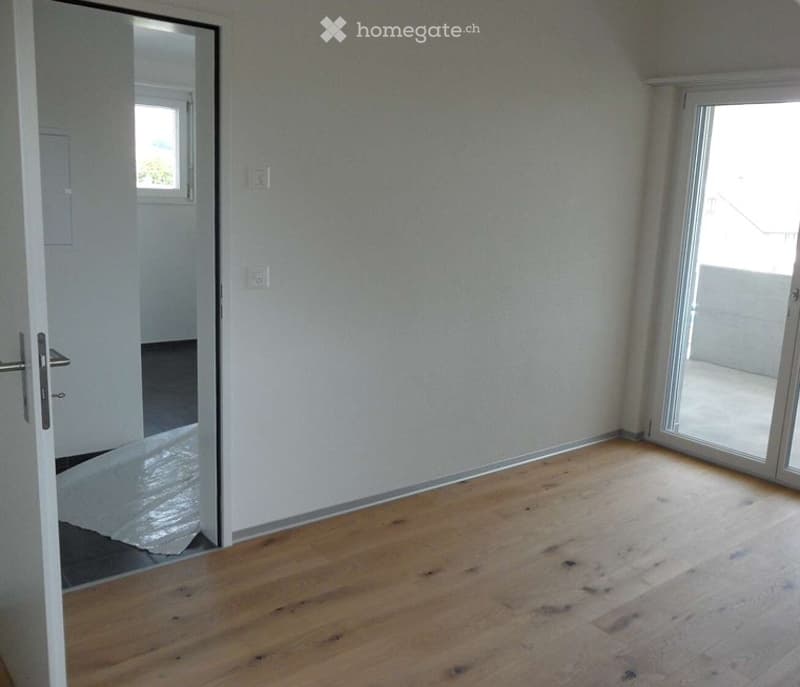 Empty room with wooden flooring, white walls, and large sliding glass door leading to a balcony.