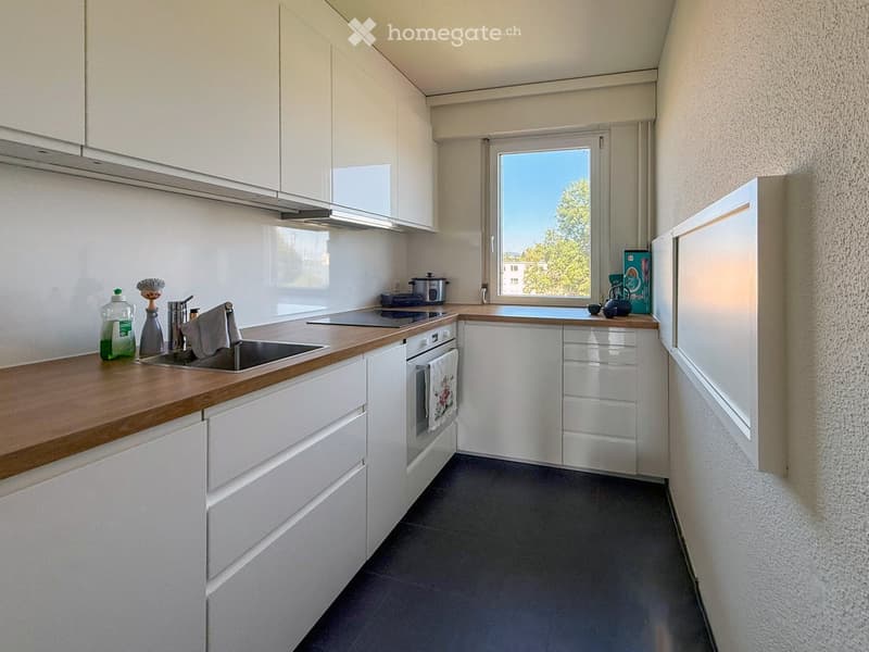 Modern kitchen with white cabinets, wooden countertops, and stainless steel appliances. Features a sink, oven, and various small items on the counter.