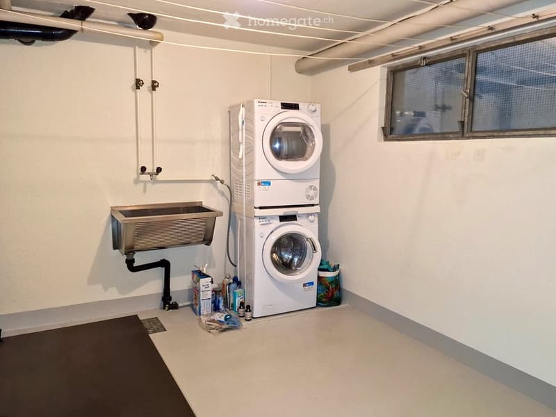 A small, clean utility room with a washing machine, dishwasher, and a sink, featuring white walls and a window.