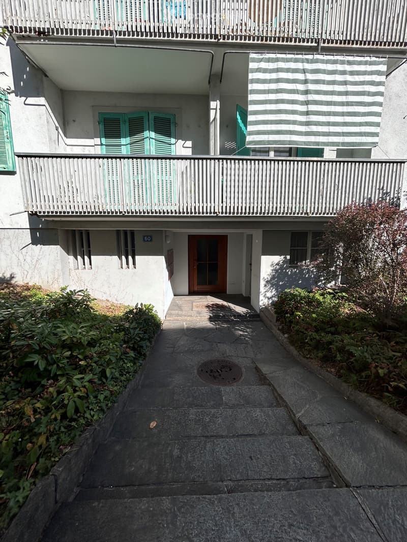 A narrow outdoor area with a staircase leading up, surrounded by white lattice fencing and greenery, with a small seating area visible at the top.