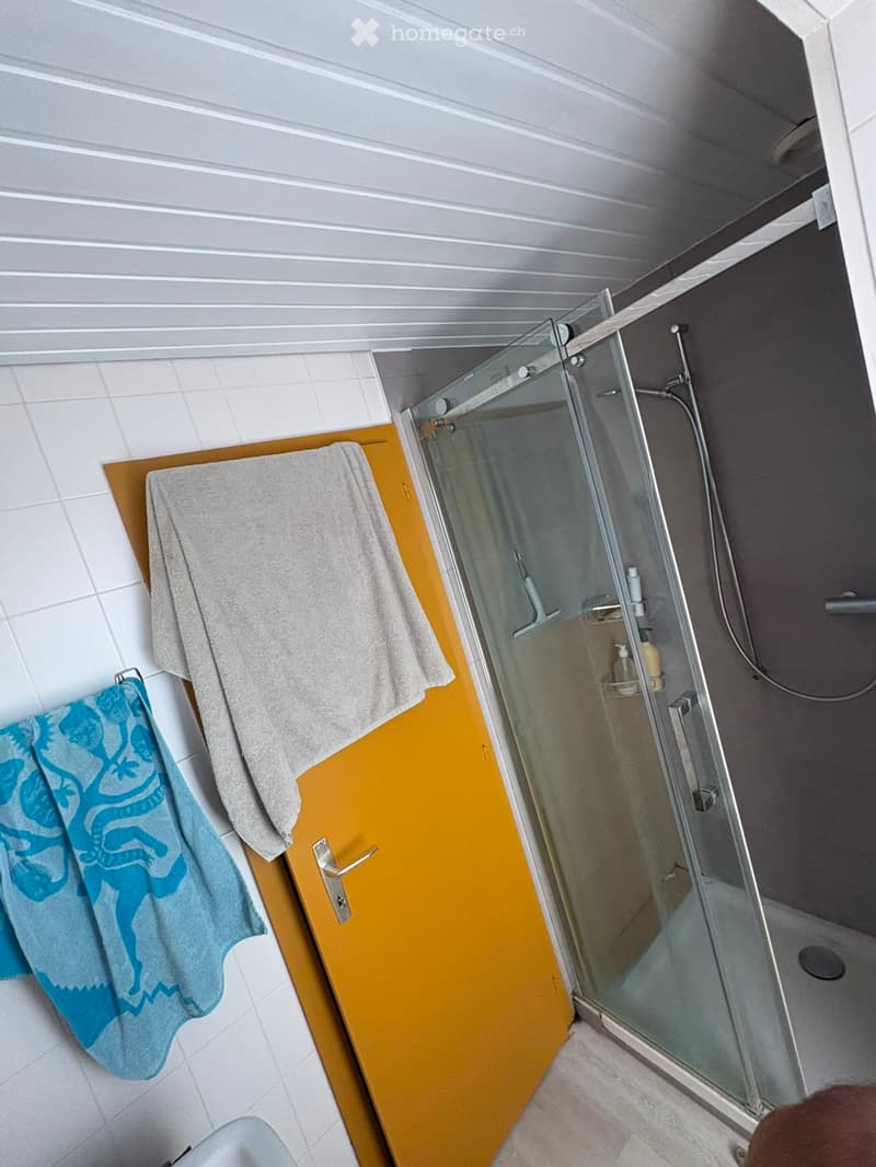 Modern bathroom with a glass-enclosed shower, white tiled walls, and a wooden cabinet with towels.