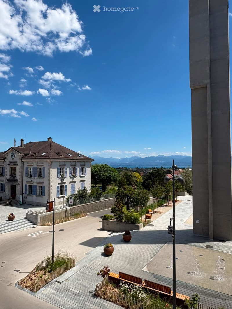 Courtyard with paved walkways, benches, potted plants, and a view of a historic building and distant mountains.