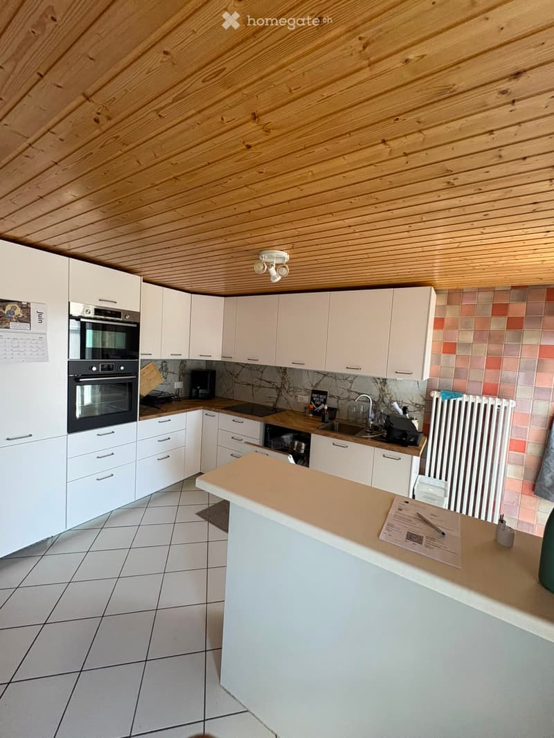 Modern kitchen with white cabinets, wooden ceiling, tiled backsplash, and a central island with a countertop.