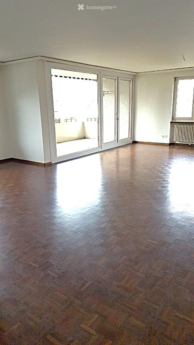 Empty room with wooden flooring, large sliding glass doors leading to a balcony, and a window on the side wall.