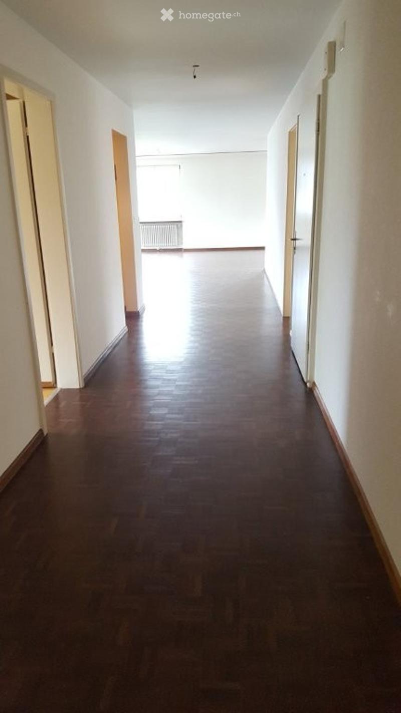 Empty hallway with polished wooden flooring and white walls, featuring several doors on both sides.