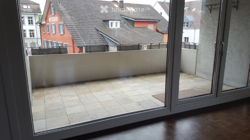 Empty balcony with tiled floor, white walls, and a view of neighboring houses.