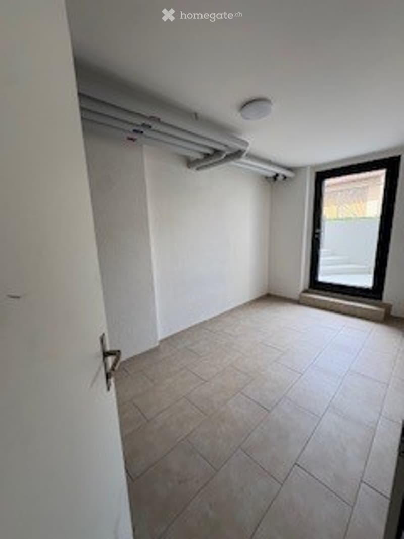Empty room with white walls, tiled floor, and a large sliding glass door leading to an outdoor area.