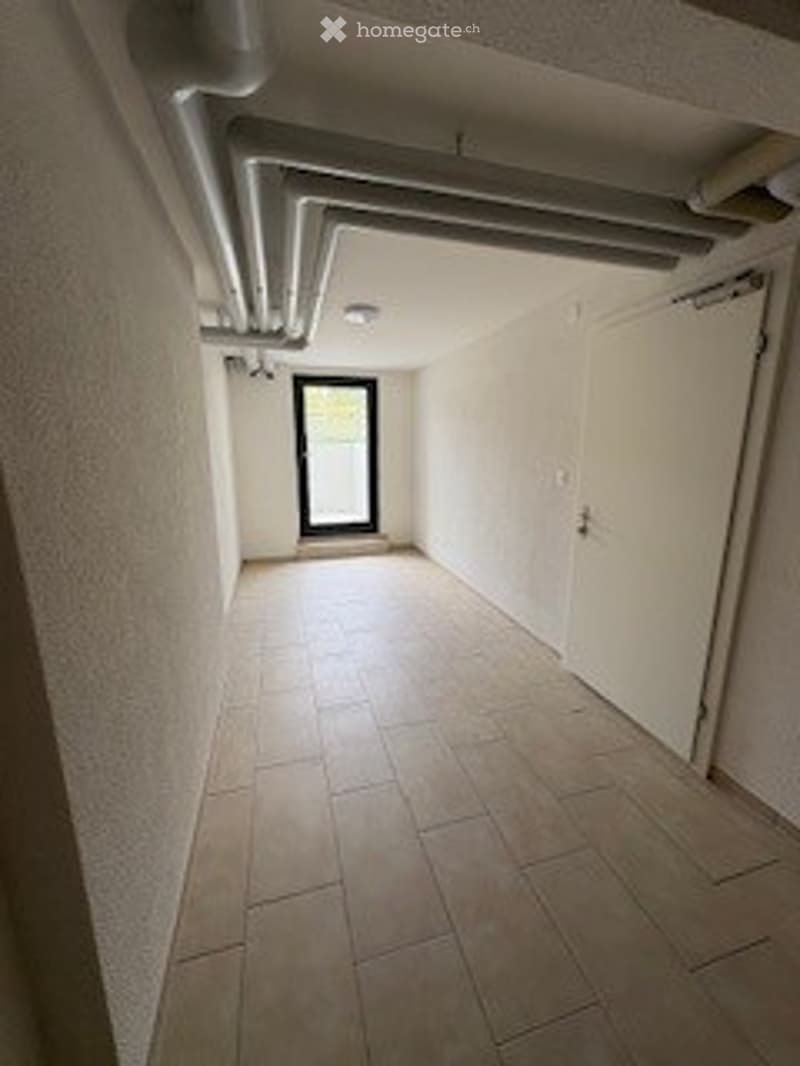 Empty hallway with tiled floor, white walls, and a door at the end.