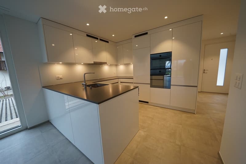 Modern kitchen with white cabinets, stainless steel sink, and built-in oven. Features a central island with a dark countertop and a sleek faucet.