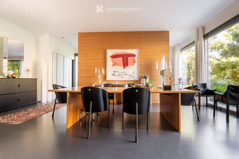 Modern dining room with a large wooden dining table surrounded by black chairs, candelabras, a painting on the wall, and a cabinet with decorative items.