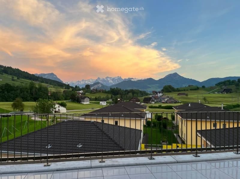 Balcony overlooking a scenic valley with houses and mountains in the background.